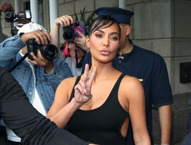 woman makes peace sign as photographers take her picture