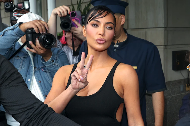 woman makes peace sign as photographers take her picture