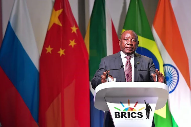 Un homme portant un costume et une cravate s'exprime sur un podium portant le logo des Brics