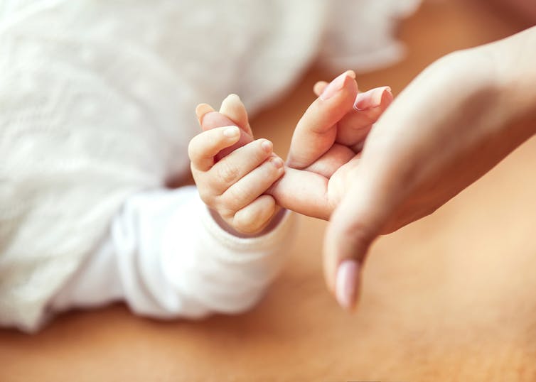 A baby holds an adult's finger