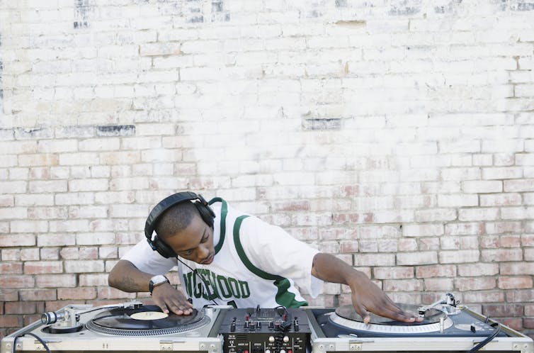 A young male deejay manipulates vinyl records on two turntables.