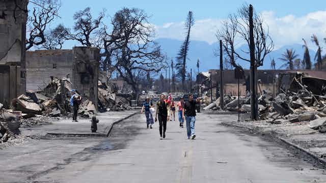 Gente caminando por la calle entre los escombros de los daños causados por el incendio forestal en Lahaina.