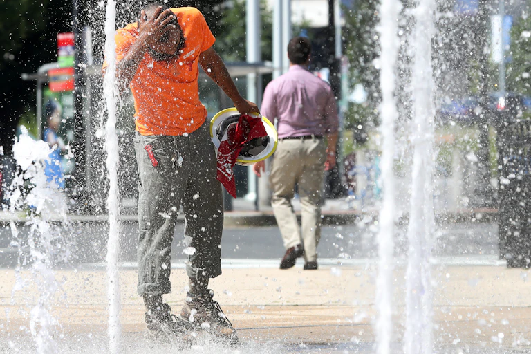 Un ouvrier du bâtiment se rafraîchit la tête dans le jet d'une fontaine située à l'extérieur d'un immeuble de bureaux.