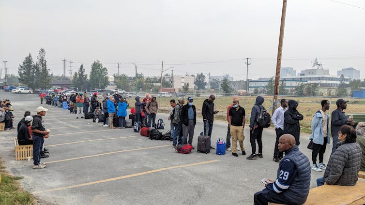 People in a long lineup with luggage in a parking lot.