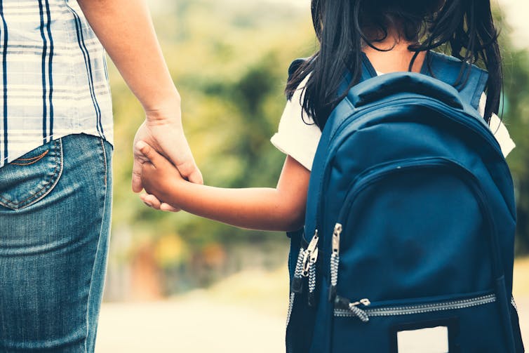 Little girl with rucksack holding father's hand