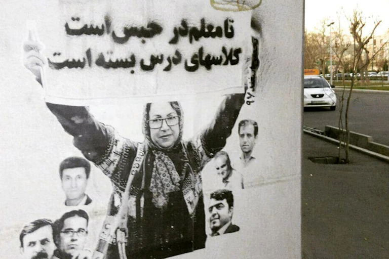 A mural on a wall shows a woman holding up a sign with Arabic writing.