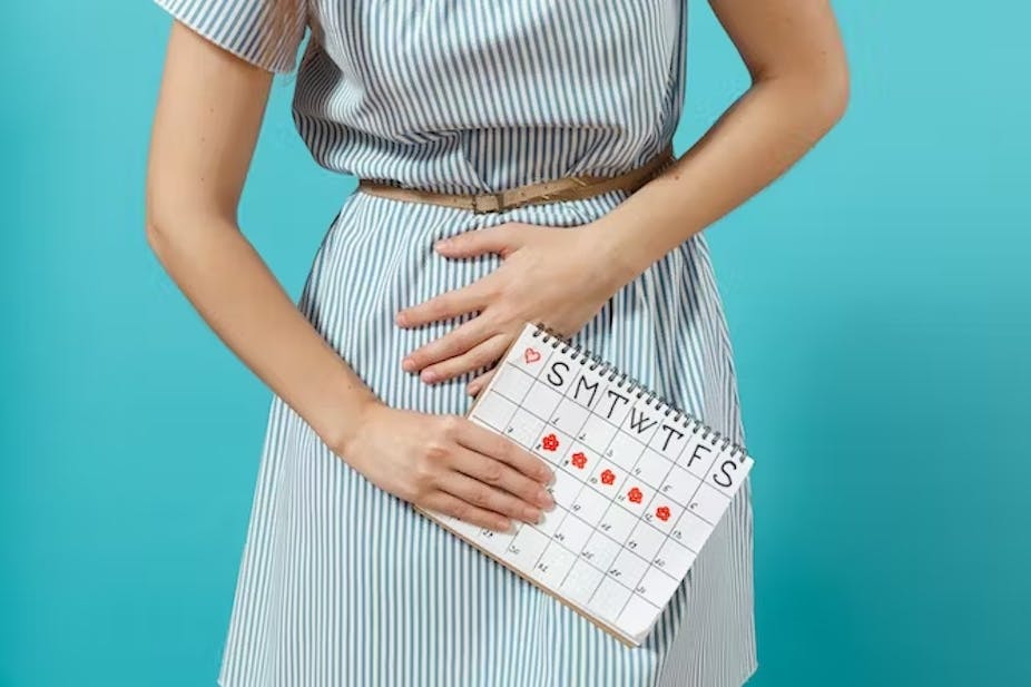 Seorang wanita memegangi perutnya yang kesakitan, sambil memegang kalender yang menunjukkan kapan haidnya akan tiba dalam sebulan.