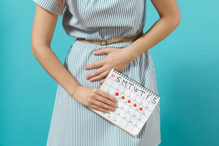 Seorang wanita memegangi perutnya yang kesakitan, sambil memegang kalender yang menunjukkan kapan haidnya akan tiba dalam sebulan.