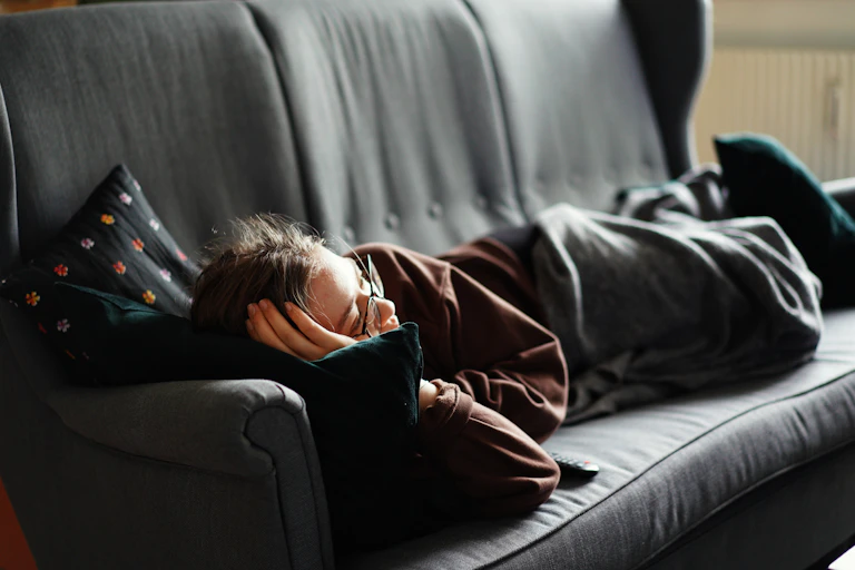 Person lays on couch with a blanket