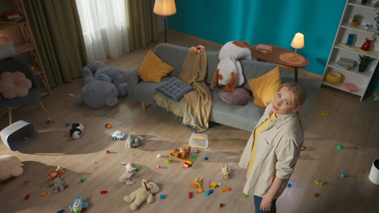 A woman looks at the camera while standing in a messy room.