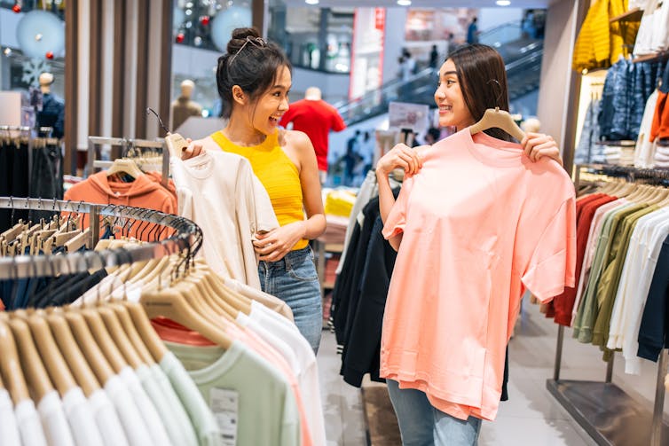 Two women showing each other shirts in a shop