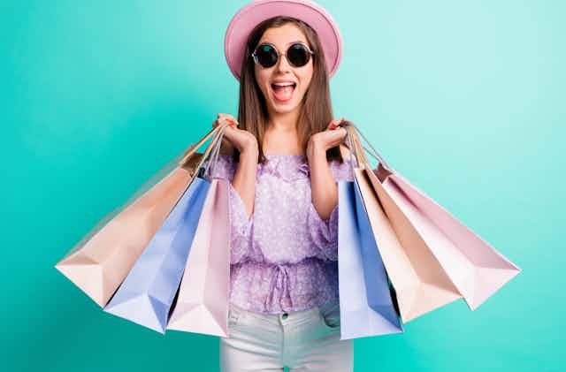 Young woman with sunglasses smiles while holding shopping bags