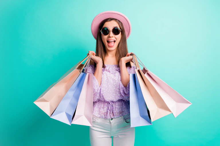 Young woman with sunglasses smiles while holding shopping bags