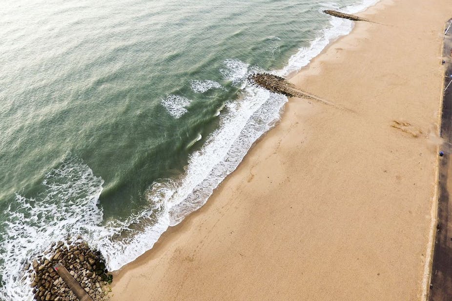 Aerial view of a sandy beach with some stony barriers protruding into the sea