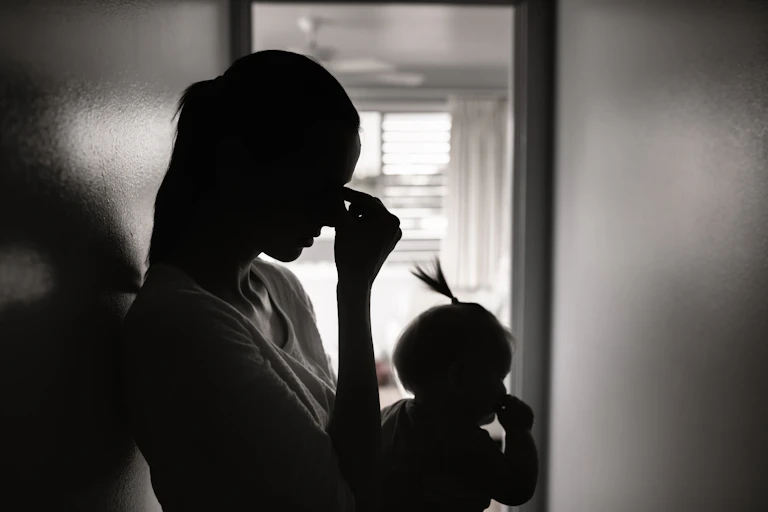 A black a white photo of a tired mother holding her baby.