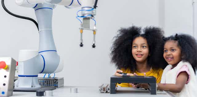 Dos niñas observan un robot mientras lo manejan con un mando teledirigido.