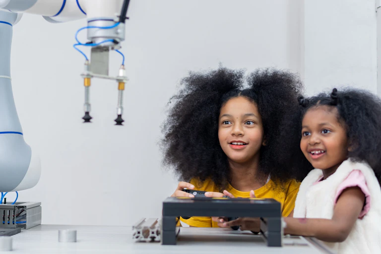 Dos niñas observan un robot mientras lo manejan con un mando teledirigido.