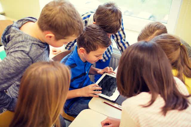 Un grupo de niños rodea a otro que está sentado y trabajando con una tableta digital.