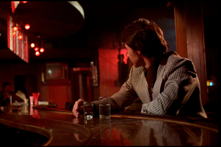 A man seated at a bar in a room lit by red neon light.