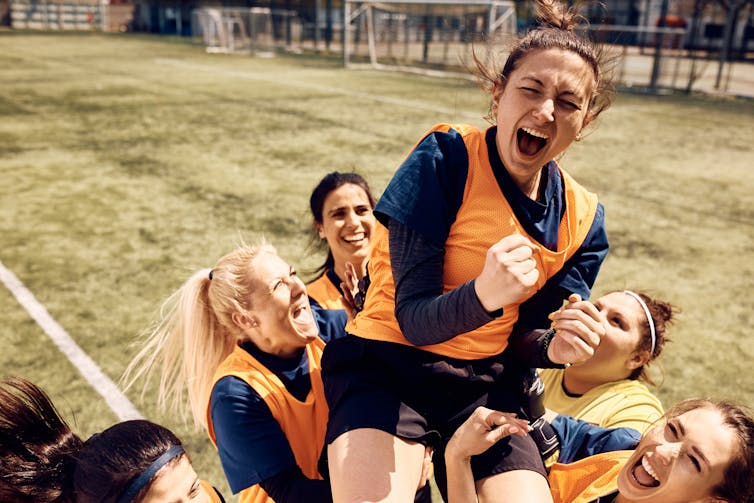 Cheerful team of female soccer players celebrating victory and carrying on of teammates who is shouting out of joy