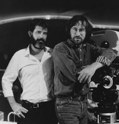 Two bearded men standing next to some film cameras.