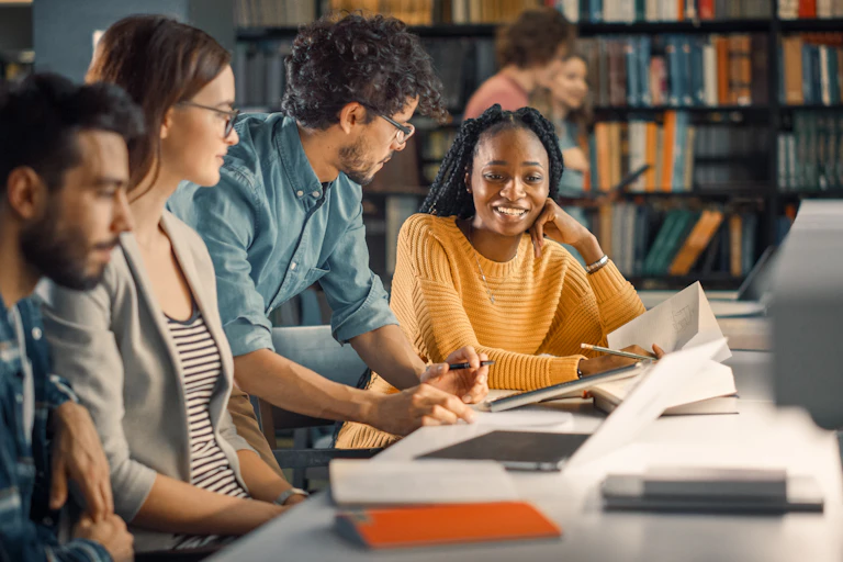 Students sit at a table in a library talking.