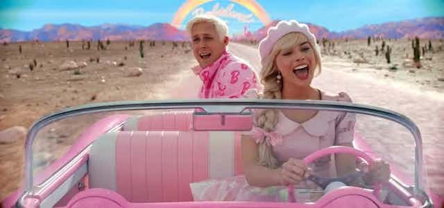 Ryan Gosling sebagai Ken dan Margot Robbie sebagai Barbie, keduanya mengenakan pakaian berwarna merah muda dan berkendara di jalan gurun. 