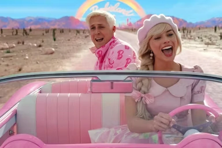 Ryan Gosling sebagai Ken dan Margot Robbie sebagai Barbie, keduanya mengenakan pakaian berwarna merah muda dan berkendara di jalan gurun.