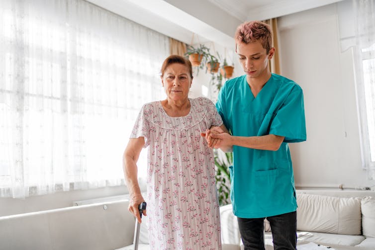 Caregiver helping older adult using cane walk in a room