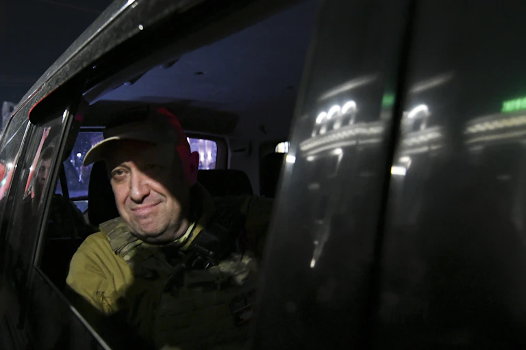 A man in military garb looks out of a car window while riding in the backseat.