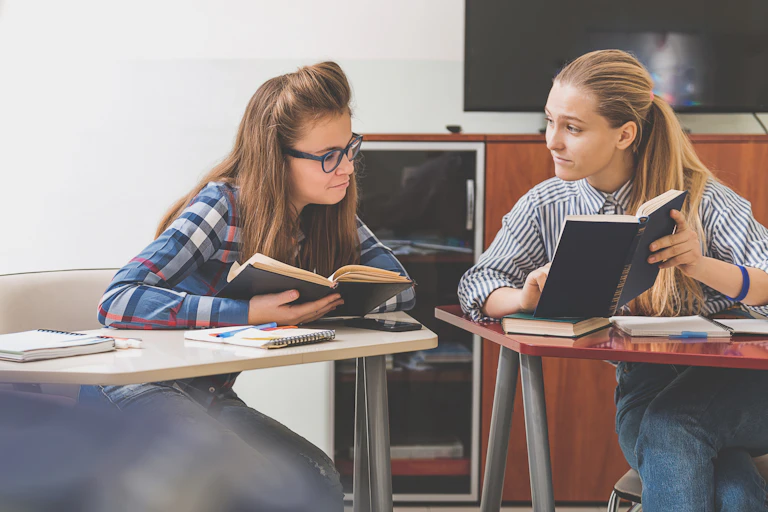 Two girls comparing textbooks in class