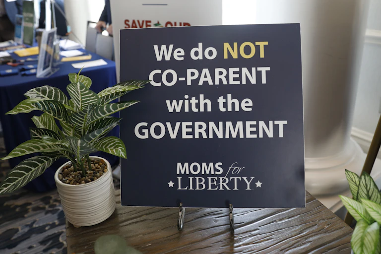 A sign that says 'We do not co-parent with the government' and 'MOMS for LIBERTY'