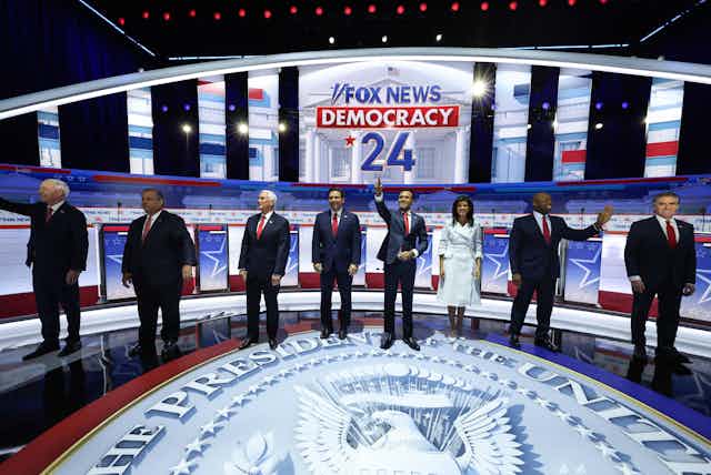 Eight people on a red, white and blue stage.