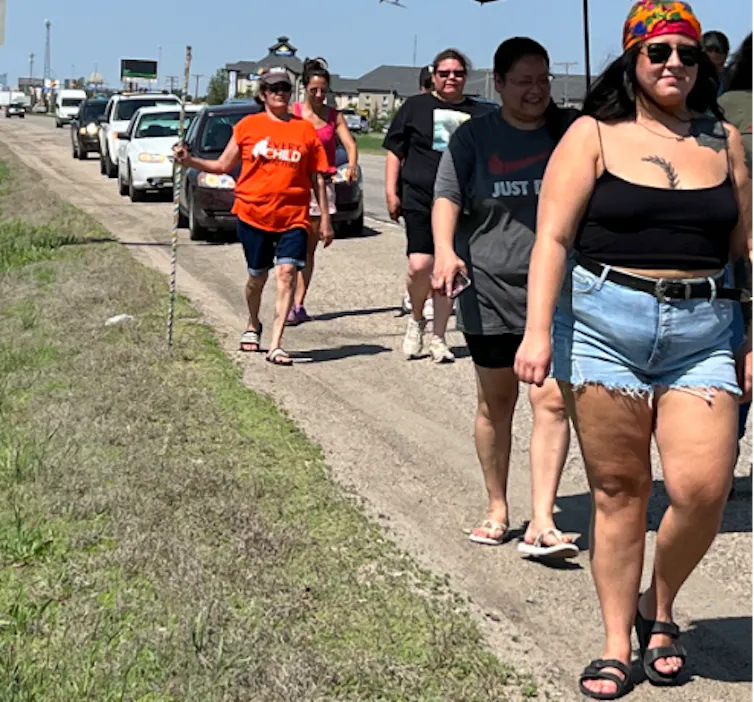 A woman walks on the highway, followed by four others and a line of cars.