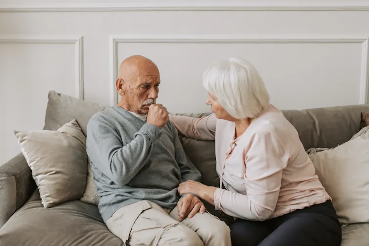 Older man coughs, while his partner looks concerned