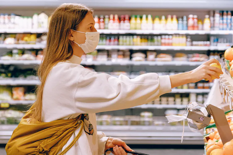 Woman at supermarket reaches for an orange
