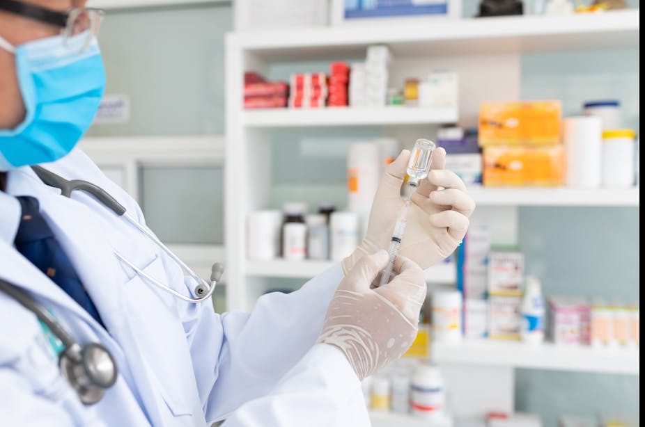 A pharmacist fills a needle with a vial of vaccine fluid.