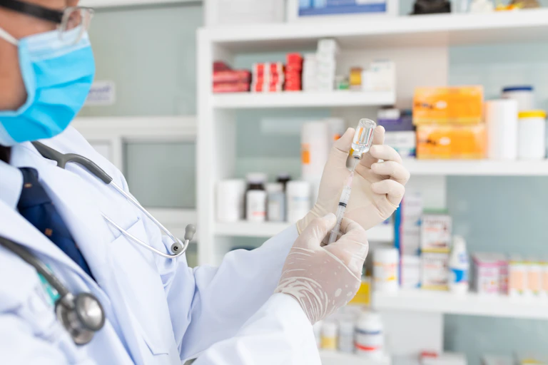 A pharmacist fills a needle with a vial of vaccine fluid.