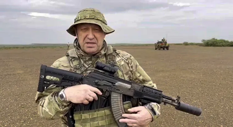Un homme en treillis de combat tient une arme d’assaut dans un champ