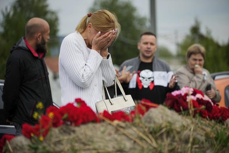 A woman cries in front of a pile of flowers.