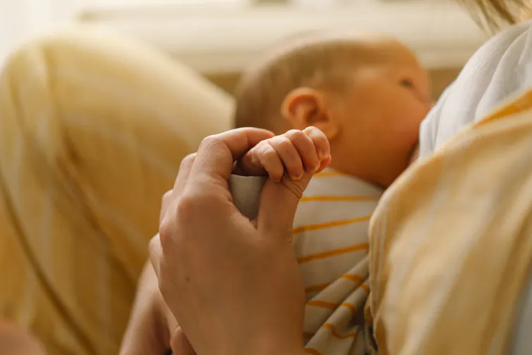 A mother holds the hand of her baby who is breastfeeding.