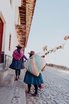 Dos mujeres caminan por una calle adoquinada vistiendo sombreros y ropas de colores.