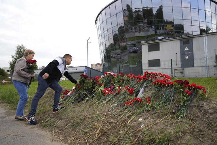 Two men lay red flowers at a makeshift memorial