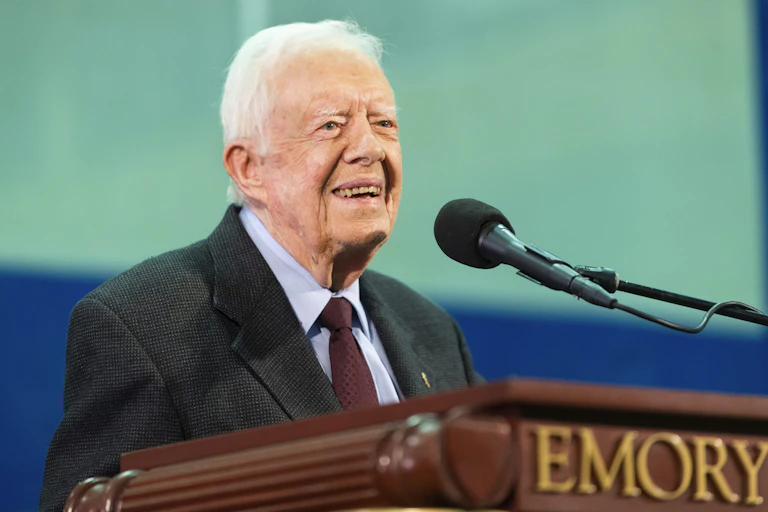 A man with grey hair smiling in front of a microphone on a podium that reads 'Emory'