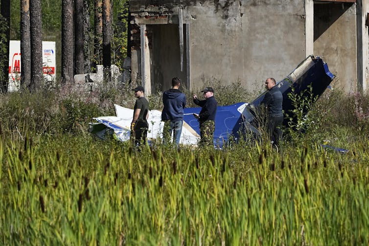 men in uniform stand around the remains of a plane in a field