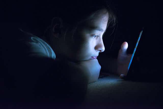 Teenager peering at their smart phone in the dark.