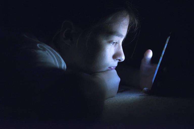 Teenager peering at their smart phone in the dark.