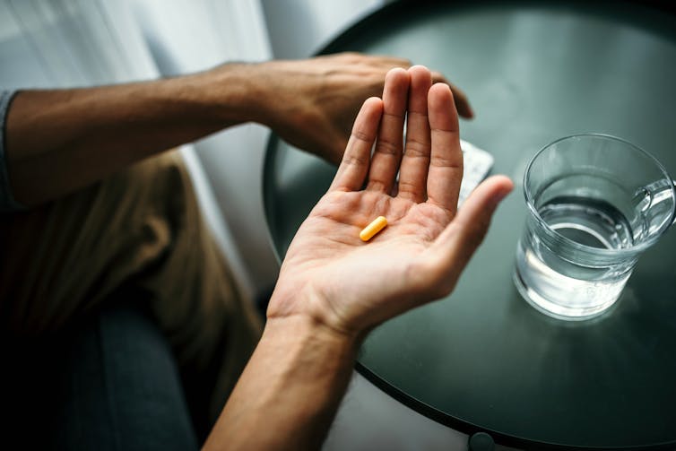 Gros plan d'une main tenant une pilule à côté d'un verre d'eau sur une table