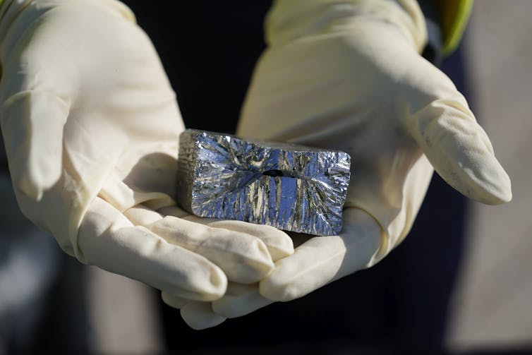 A block of a silvery mineral is held in gloved hands