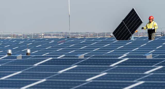 A construction worker installs a solar panel on a huge roof